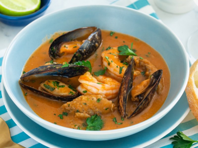 Un tazón con sopa de pescado francesa bullabesa. Junto a él, dos rebanadas de baguette.