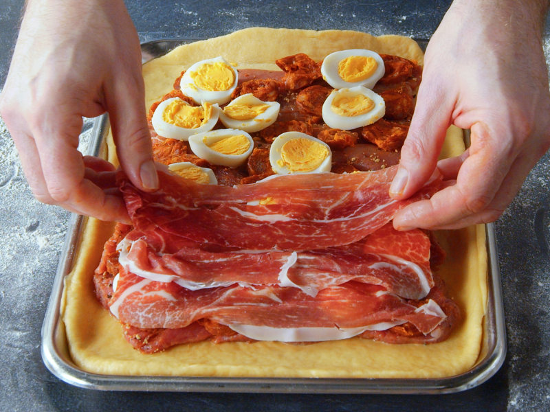 Un cocinero cubre la base de una empanada de carne española con jamón.