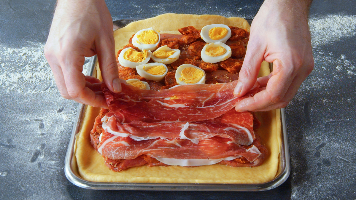 Un cocinero cubre la base de una empanada de carne española con jamón.
