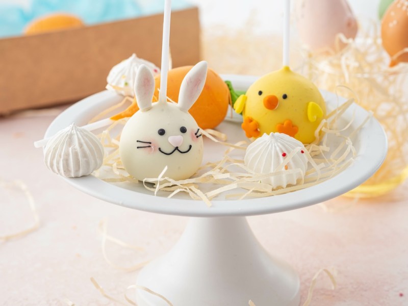 Cake pop de conejito de Pascua y cake pop de pollito en un plato de tarta con más decoración.