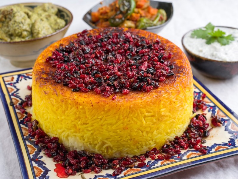 Arroz persa tahdig en un plato estampado, decorado con frutos secos, detrás cuencos con pequeños aperitivos.
