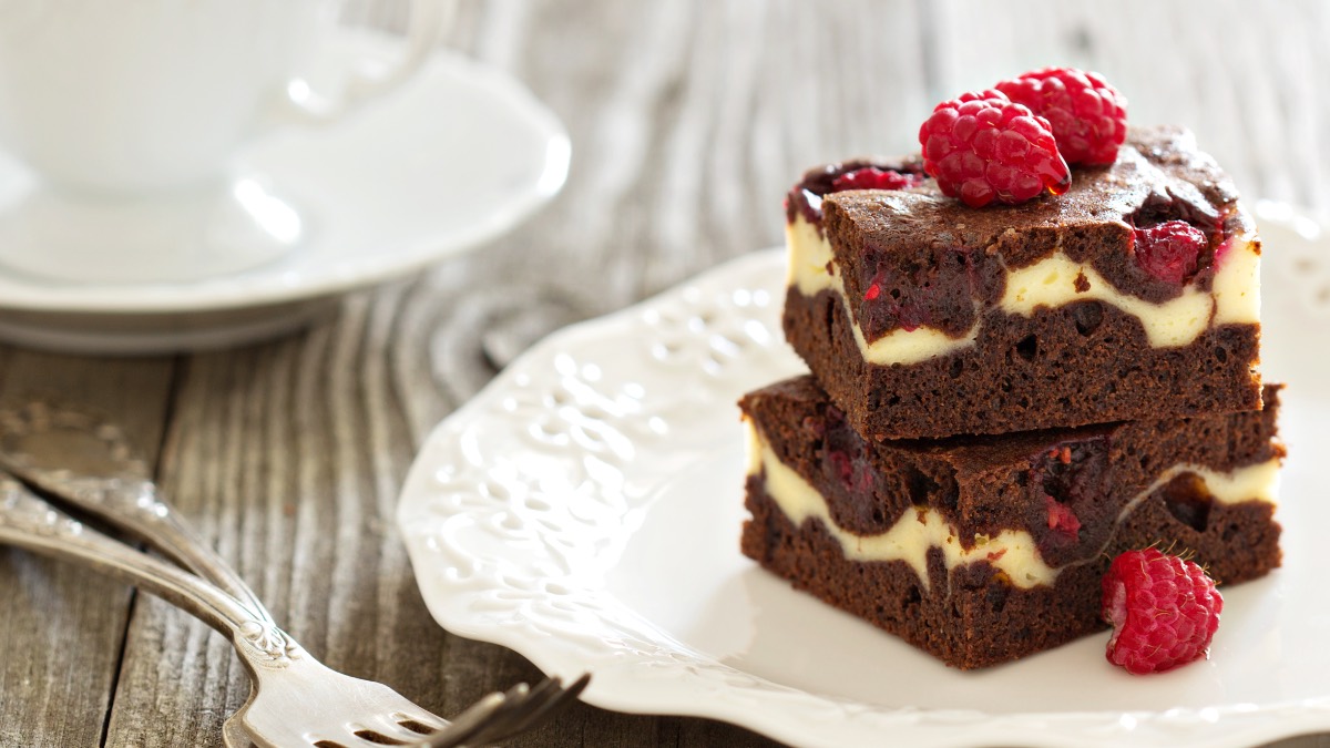Dos brownies de cheesecake con frambuesas uno encima del otro en un plato.