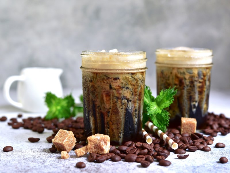 2 vasos de frappé griego, rodeados de cubos de azúcar y granos de café.