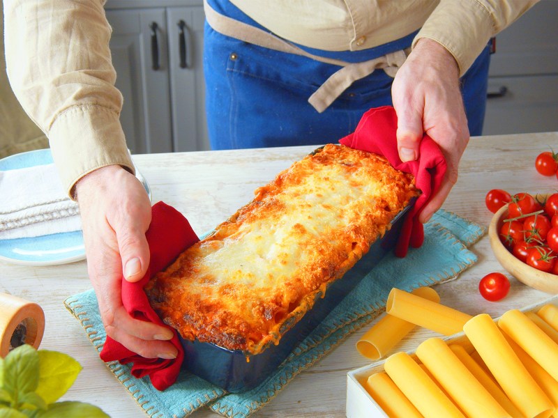 Un cocinero presenta una fuente para horno con canelones rellenos de mozzarella.