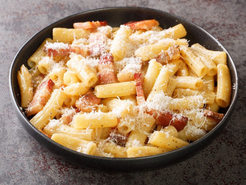 Un plato de pasta a la gricia sobre un fondo oscuro.