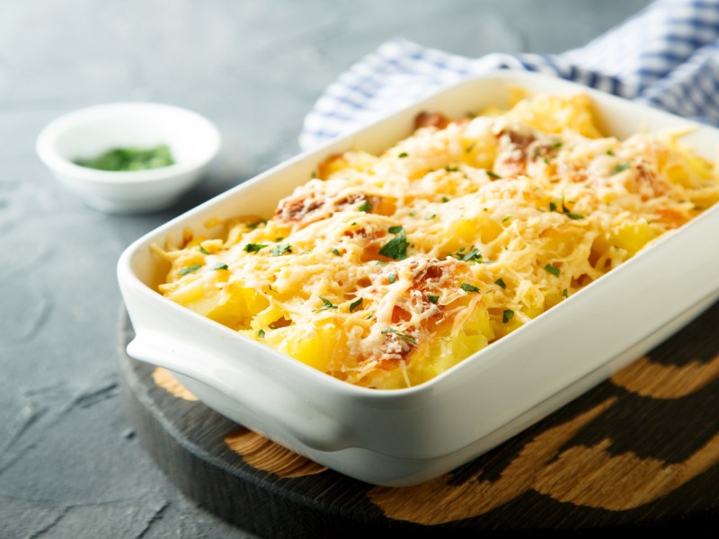 Coliflor gratinada en una fuente blanca para horno, que está sobre una tabla.