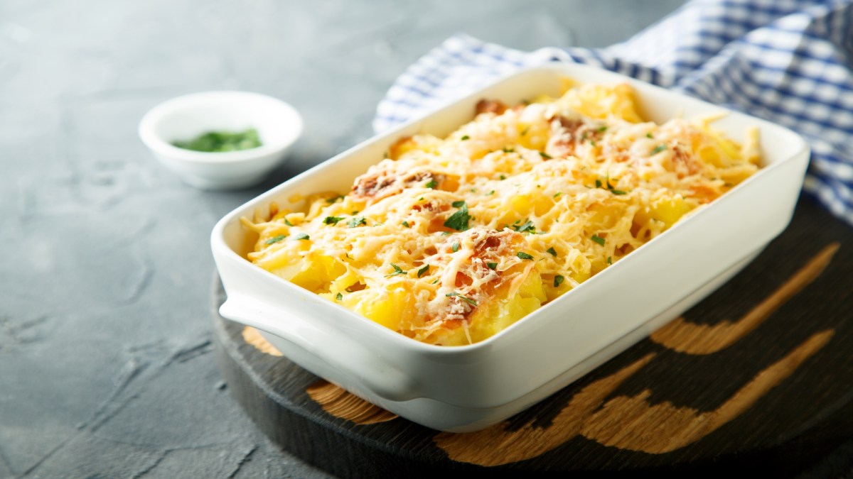 Coliflor gratinada en una fuente blanca para horno, que está sobre una tabla.