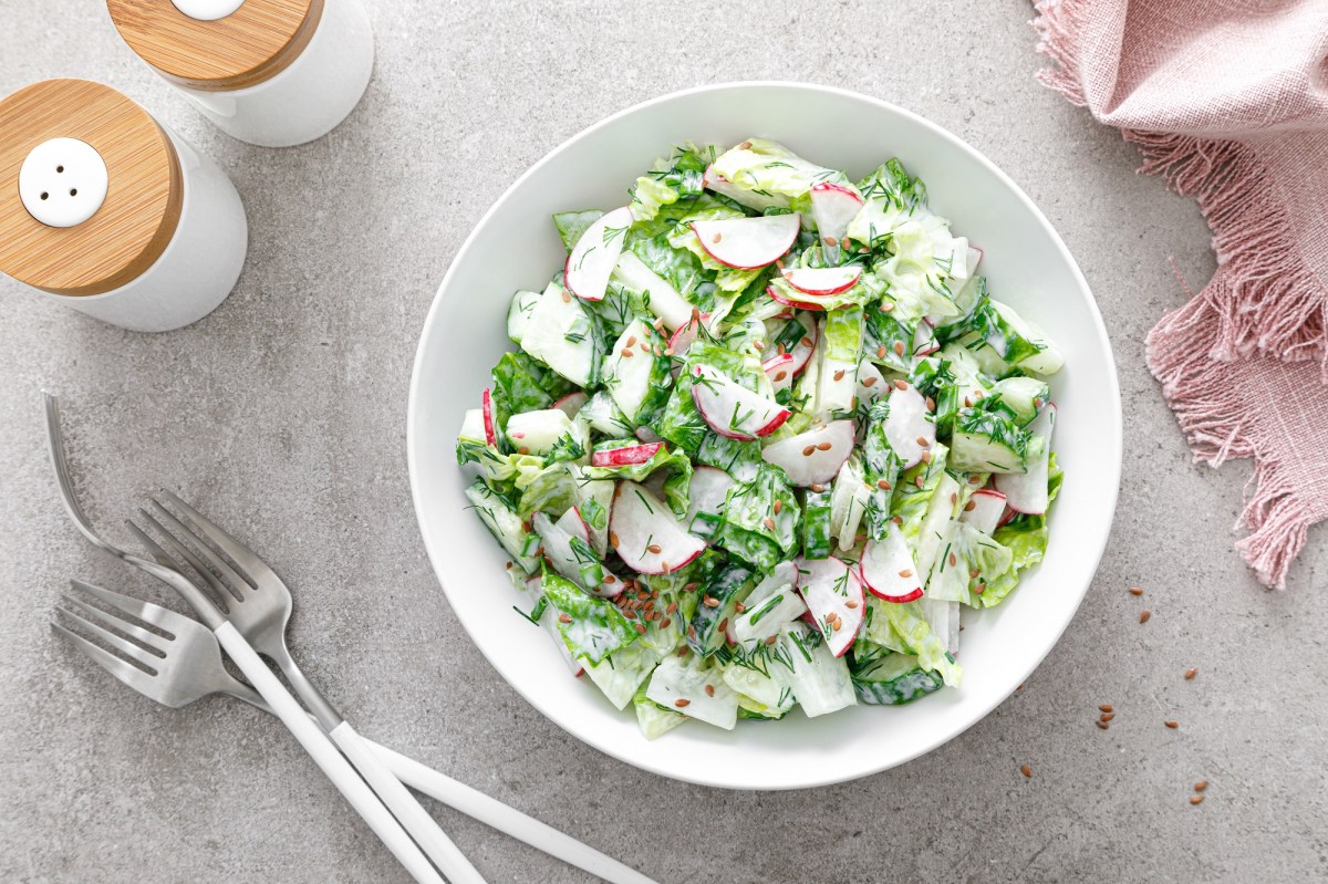 Tazón de ensalada con rábanos y pepinos sobre una mesa clara y cubiertos.