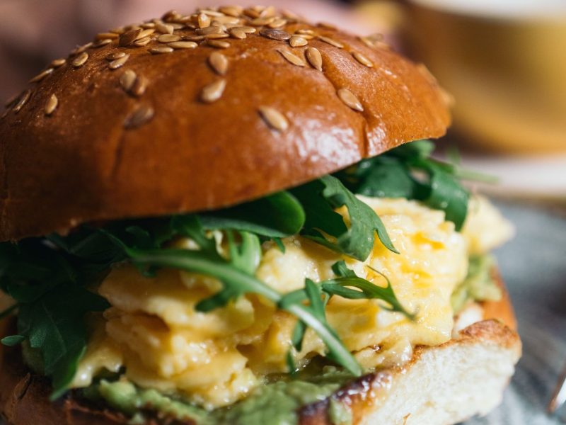 Hamburguesa de desayuno con huevos revueltos y rúcula, servida en un plato.