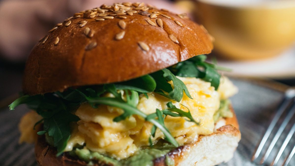 Hamburguesa de desayuno con huevos revueltos y rúcula, servida en un plato.