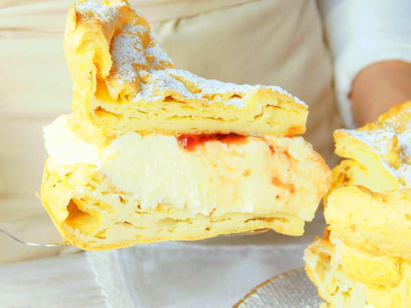 Rebanada de karpatka se está sacando del pastel completo.