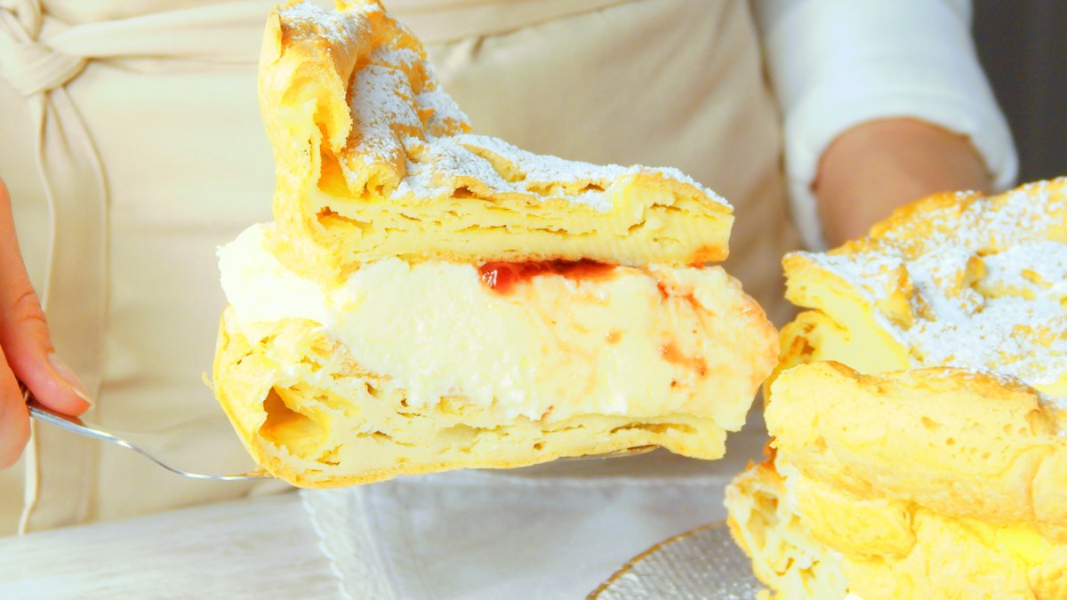 Rebanada de karpatka se está sacando del pastel completo.
