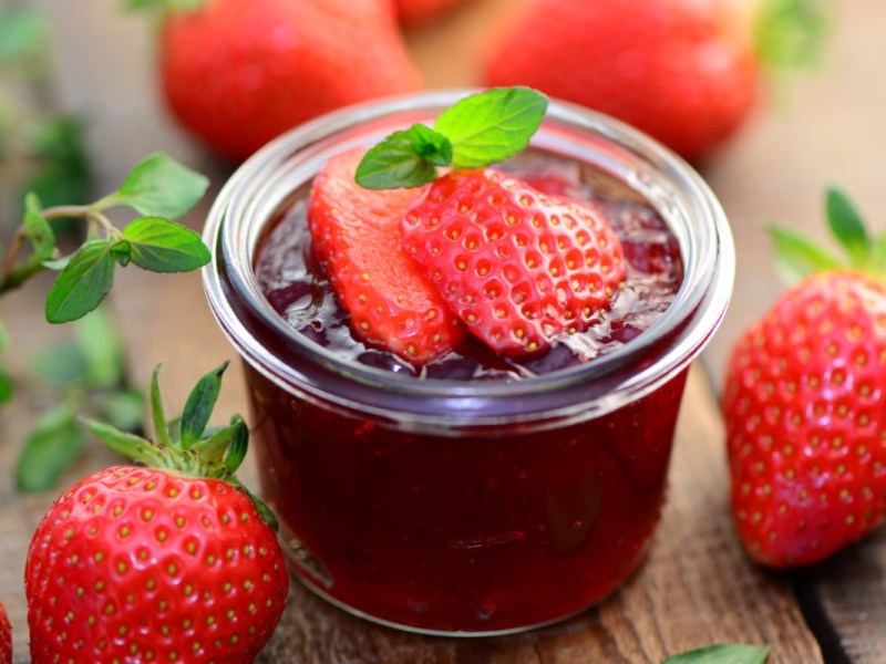 Un frasco de mermelada de fresa y menta con fresas frescas por encima. Alrededor hay fresas.