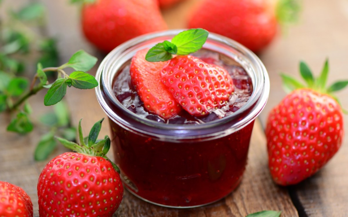 Un frasco de mermelada de fresa y menta con fresas frescas por encima. Alrededor hay fresas.