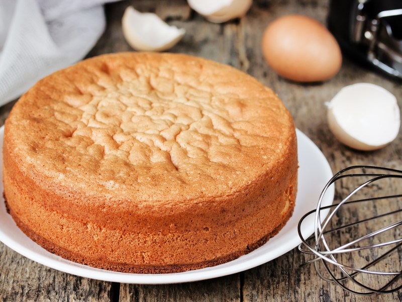 Pastel de mazapán de dos ingredientes en un plato blanco. Detrás hay cáscaras de huevo y un batidor.