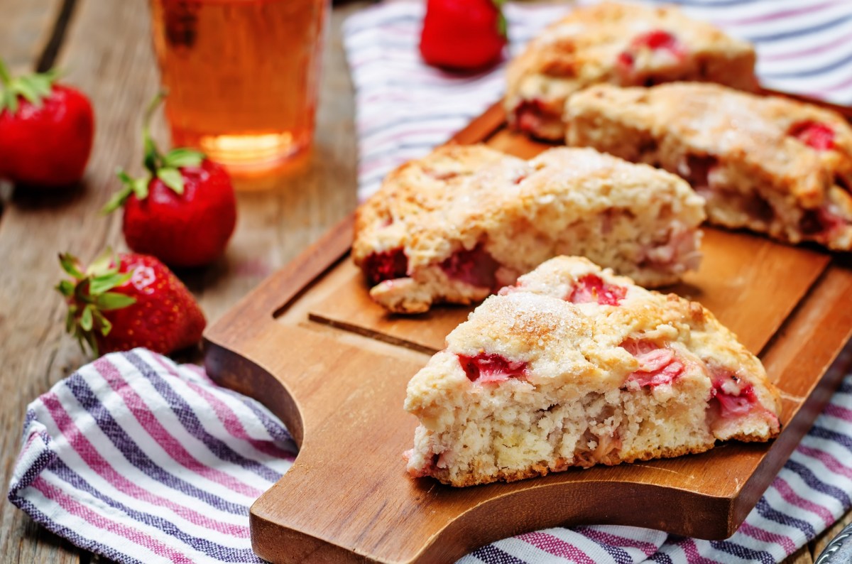 Scones de fresa y suero de leche en una tabla, fresas y un paño de cocina a rayas.