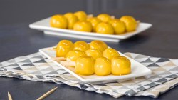 Tres brochetas de dango se encuentran en un plato blanco. Al fondo se ven más brochetas de dango. Están cubiertas con un glaseado dorado.