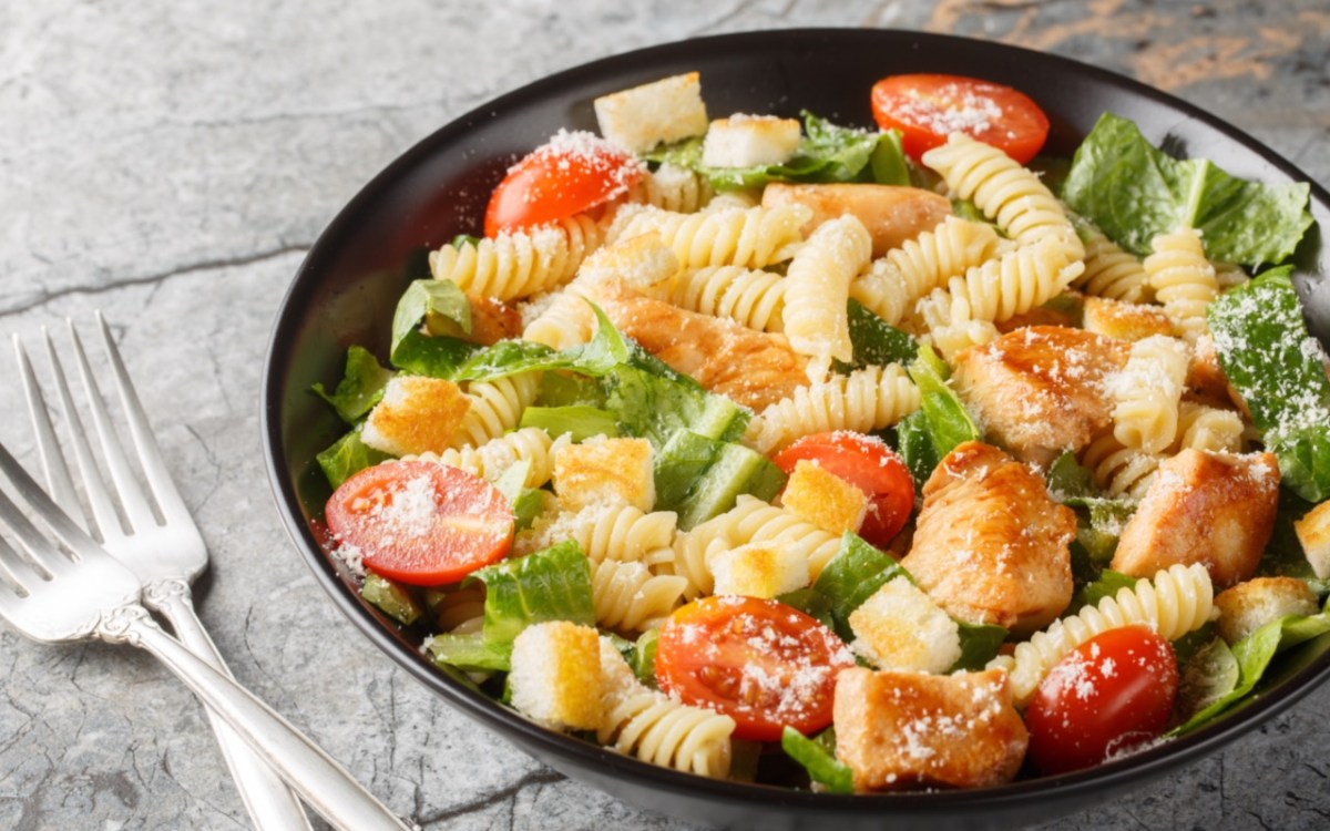 Un plato de ensalada César con pasta, junto al cual hay dos tenedores.