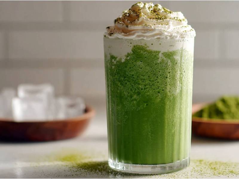 Vaso de frappuccino de matcha sobre una mesa, tazón de cubos de hielo al lado