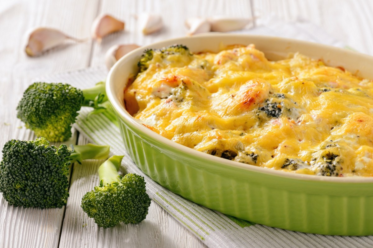 Una fuente para horno con pastel de brócoli y papa, junto a ramitos de brócoli y dientes de ajo.