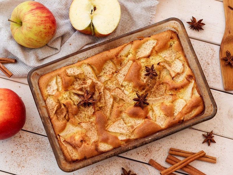Pastel de manzana en una fuente para hornear rectangular, vista superior. Alrededor hay manzanas, ramas de canela y estrellas de anís.