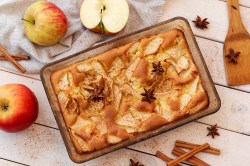 Pastel de manzana en una fuente para hornear rectangular, vista superior. Alrededor hay manzanas, ramas de canela y estrellas de anís.